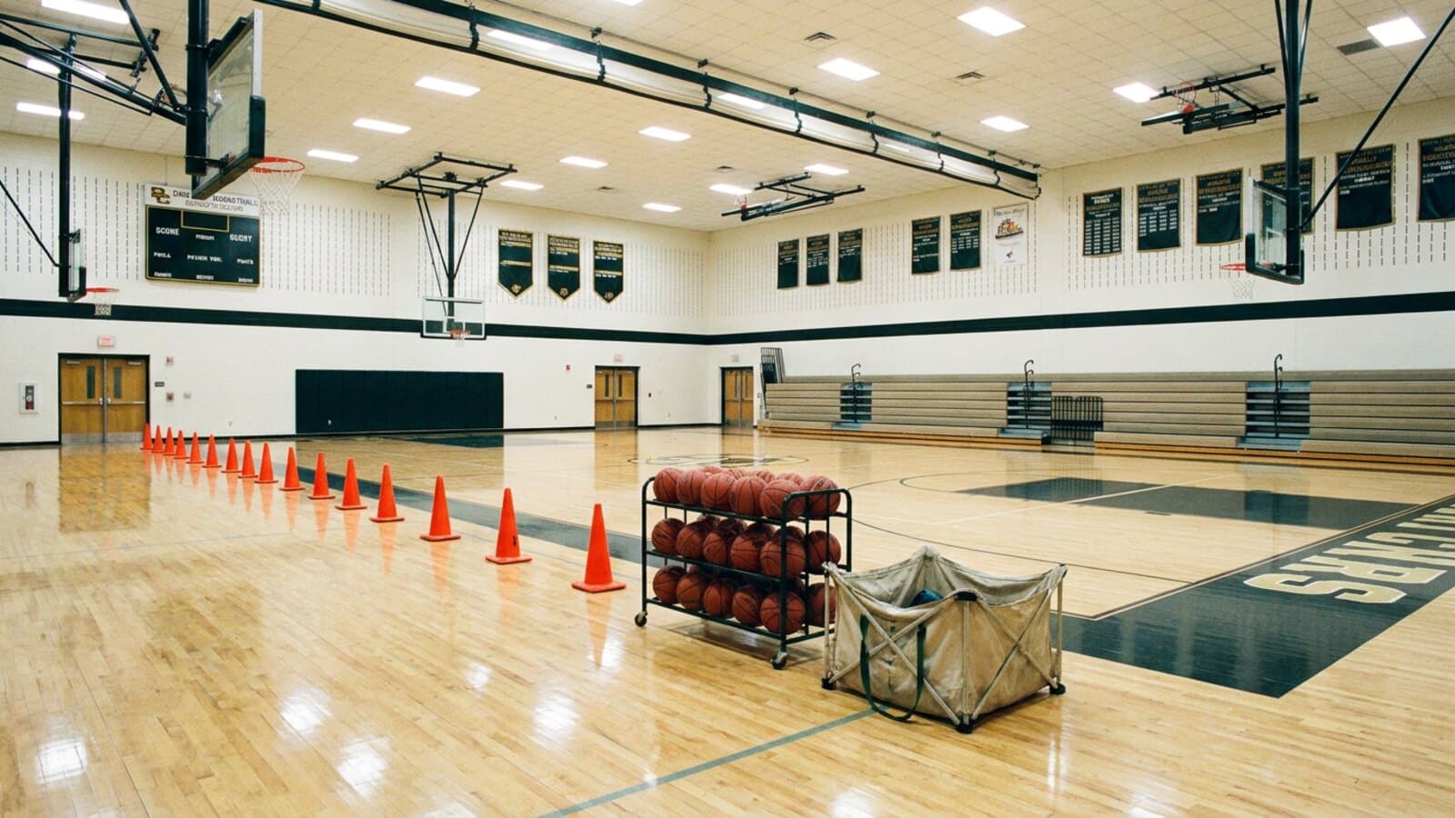 A full indoor basketball court set up for team practice with cones and a ball rack on the sideline